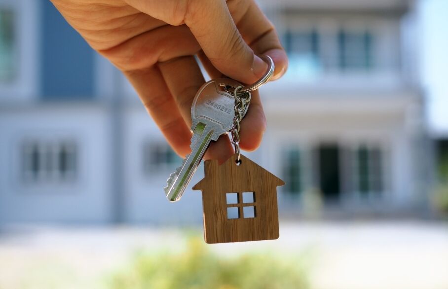 A hand holding a key in front of house