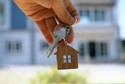 A hand holding a key in front of house